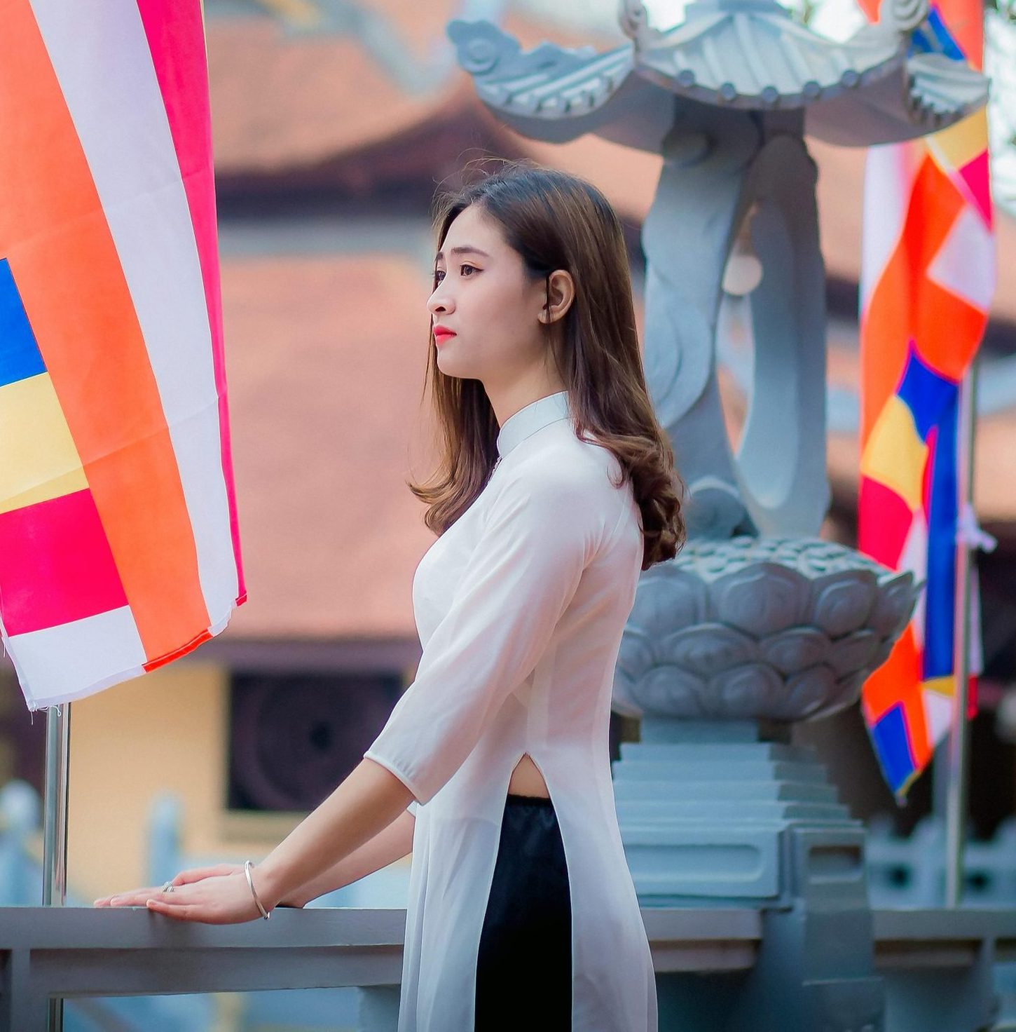 Elegant woman in traditional dress standing beside colorful flags at a temple.